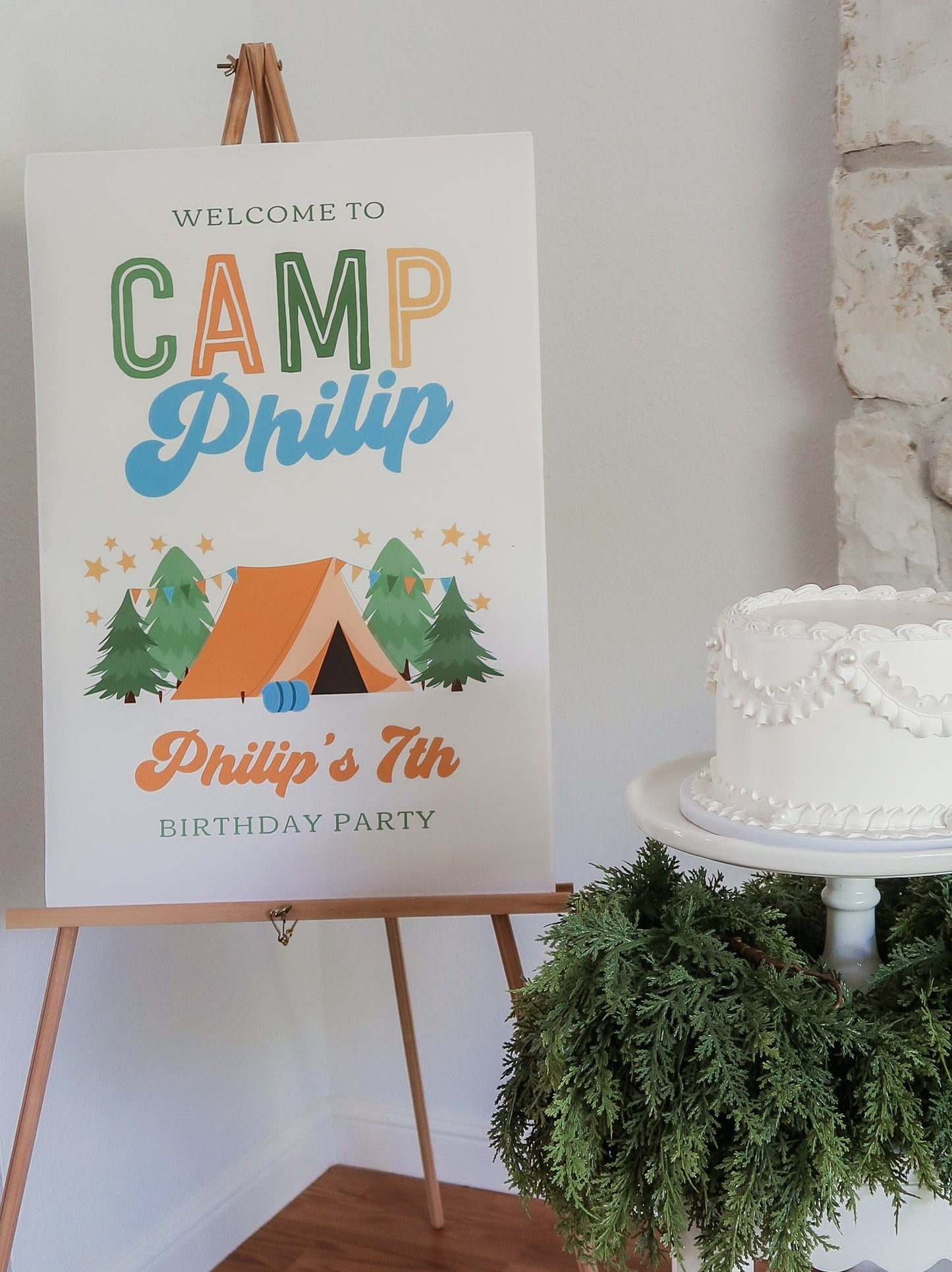 Birthday party sign for 'Camp Philip' with a cake and greenery in the background.