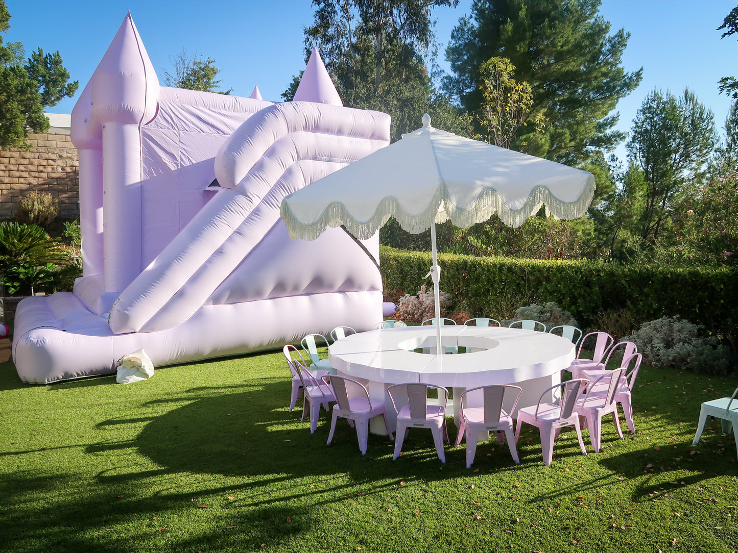 Scalloped kids round table with lavender metal chairs under a white umbrella beside a bounce house in Calabasas, CA.