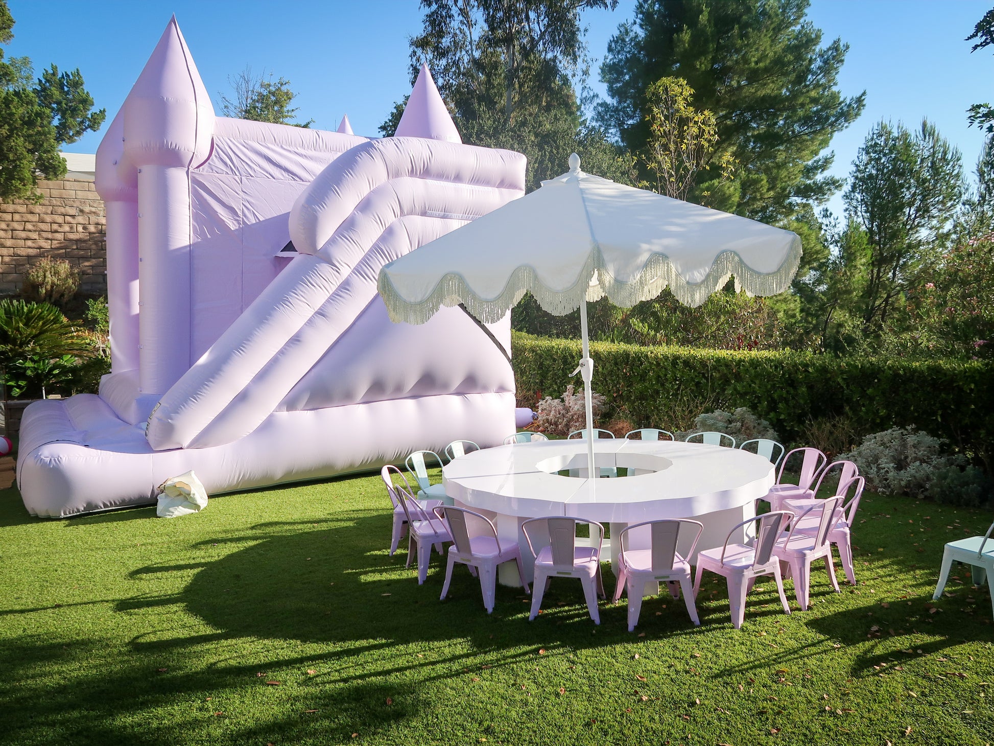 Scalloped kids round table with lavender metal chairs under a white umbrella beside a bounce house in Calabasas, CA.