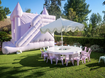 Scalloped kids round table with lavender metal chairs under a white umbrella beside a bounce house in Calabasas, CA.