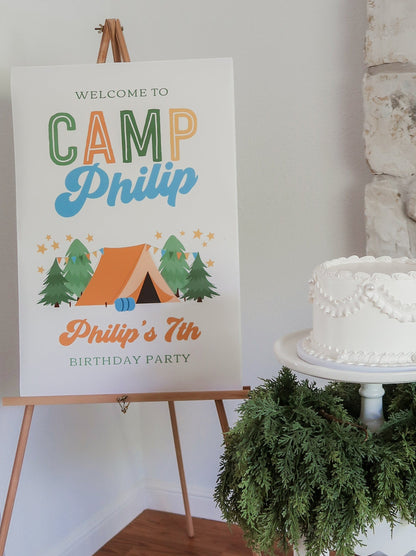 Birthday party sign for 'Camp Philip' with a cake and greenery in the background.