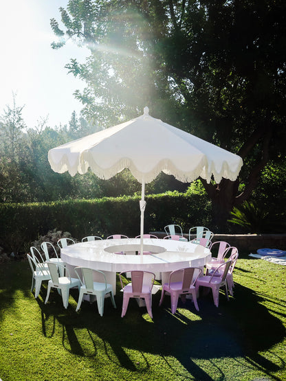 Scalloped kids dining table with pastel metal chairs under a white fringe umbrella in Calabasas, CA.